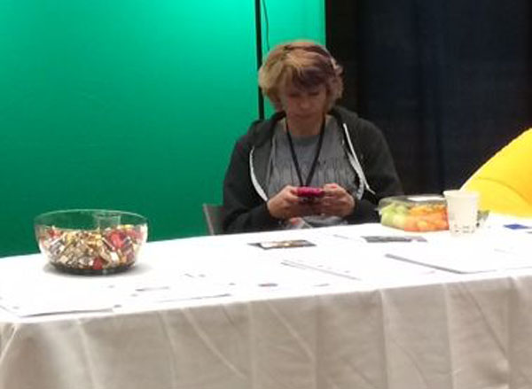 Bored looking person on their mobile phone sitting behind at table at a trade show.
